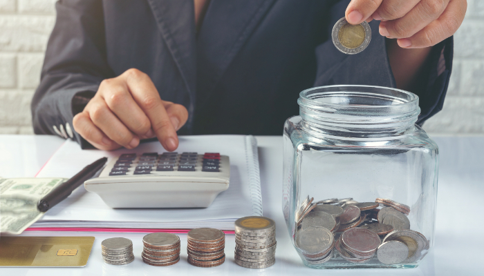 mano introduce moneda en tarro de cristal en la mesa con calculadora y más dinero