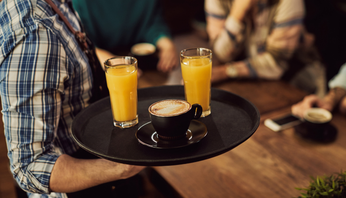 camarero con la bandeja de zumos y café sirviendo a clientes en una cafetería