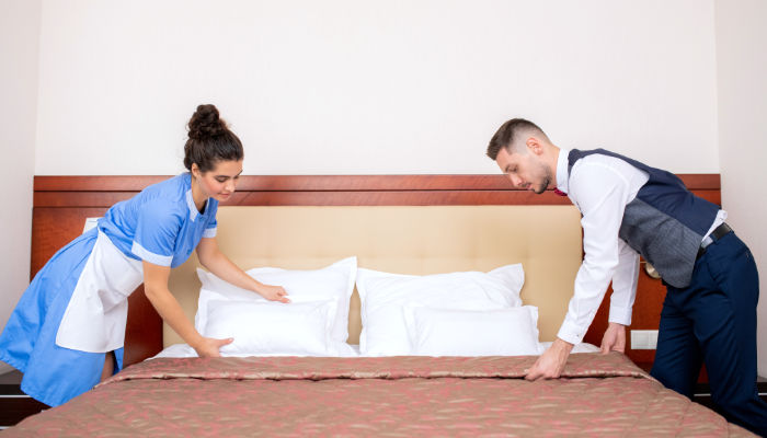 chica y chico arreglando una cama de habitación de hotel