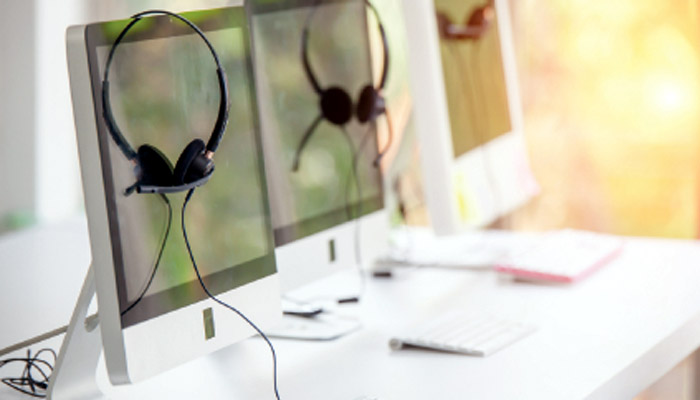 imagen de puestos de trabajo; mesa con sus pc y auriculares con micro