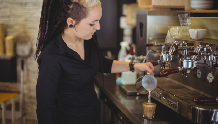 camarera vertiendo leche en taza de café mostrador