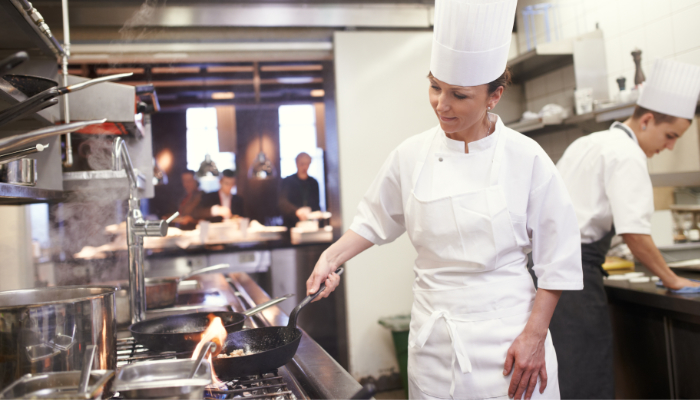 chef mujer muy profesional saltea la comida con una sartén en la cocina de un restaurante que prepara comida de catering, comida de alta calidad, etc