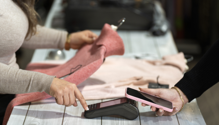 en el mostrador de una tienda de ropa un cliente que paga con su smartphone